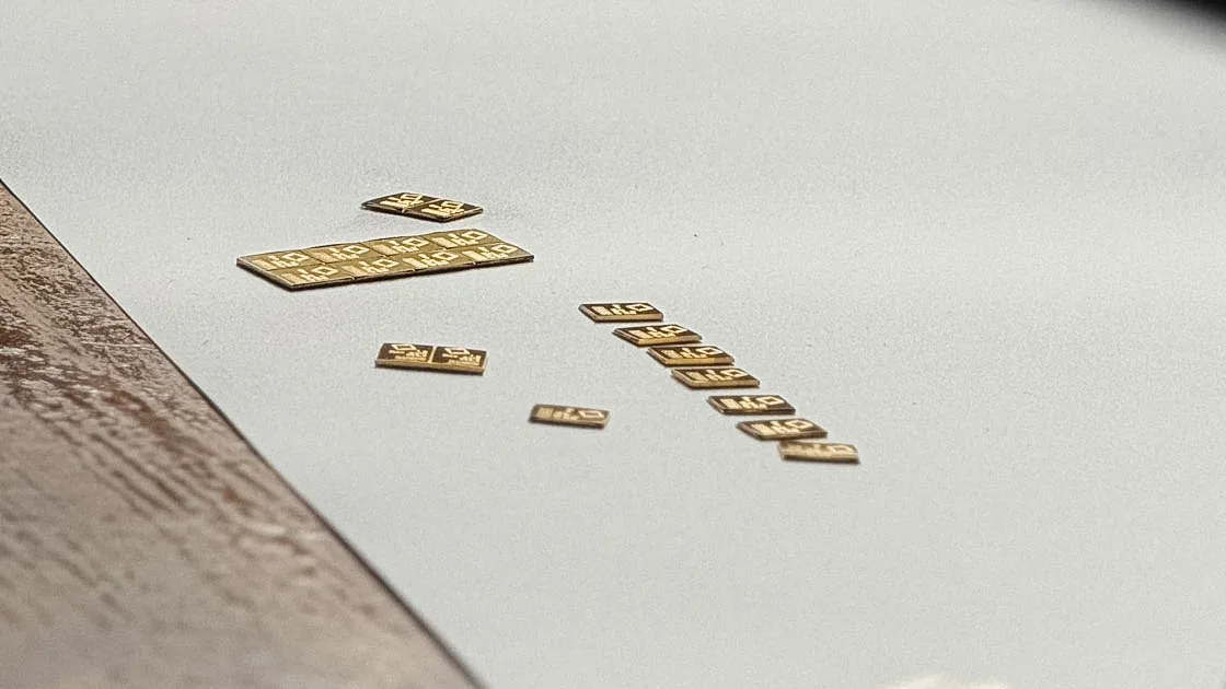 Gold bars of several sizes laid out on a workbench, a watch strap in the background
