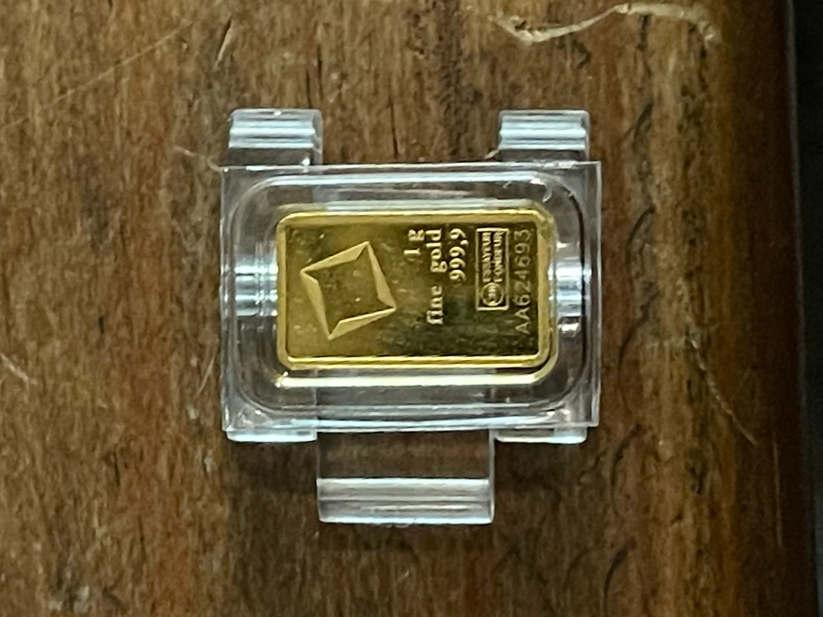 A one-gram gold bar seated in a clear prototype capsule on a wooden table